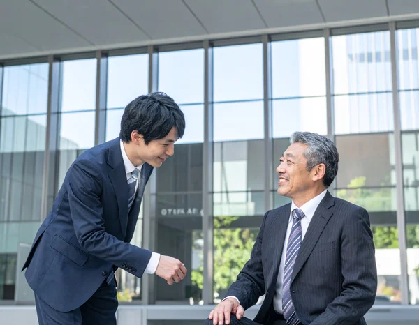 Japanese coworkers greeting each other politely with 'Otsukaresama desu' in a modern office